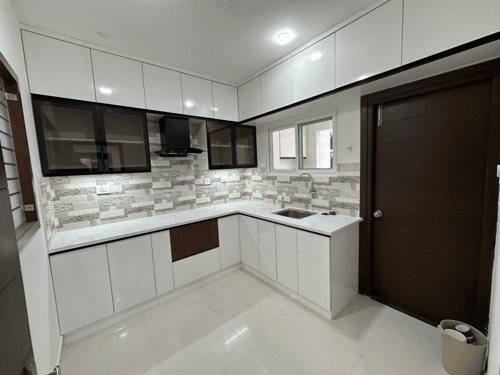 L-shaped modular kitchen with white cabinets, mosaic tile backsplash and integrated chimney by SB Interior Solutions Hyderabad