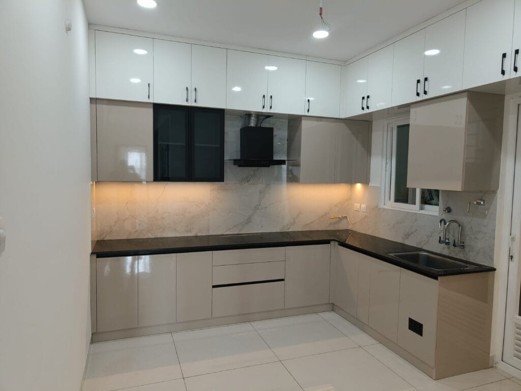 L-shaped modular kitchen with gloss white upper cabinets and dark grey lower cabinets by SB Interior Solutions Hyderabad